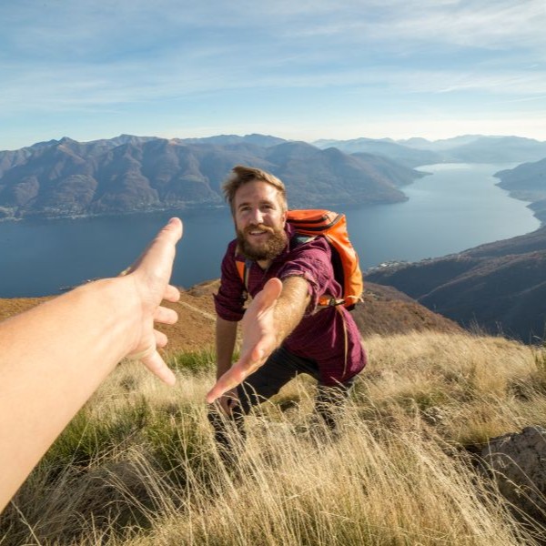 Mann beim Bergsteigen reicht Hand zur Hilfe