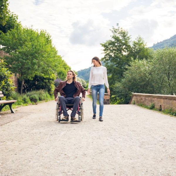 Junges Paar unterwegs – Mann im Rollstuhl genießt Spaziergang im Freien mit Partnerin